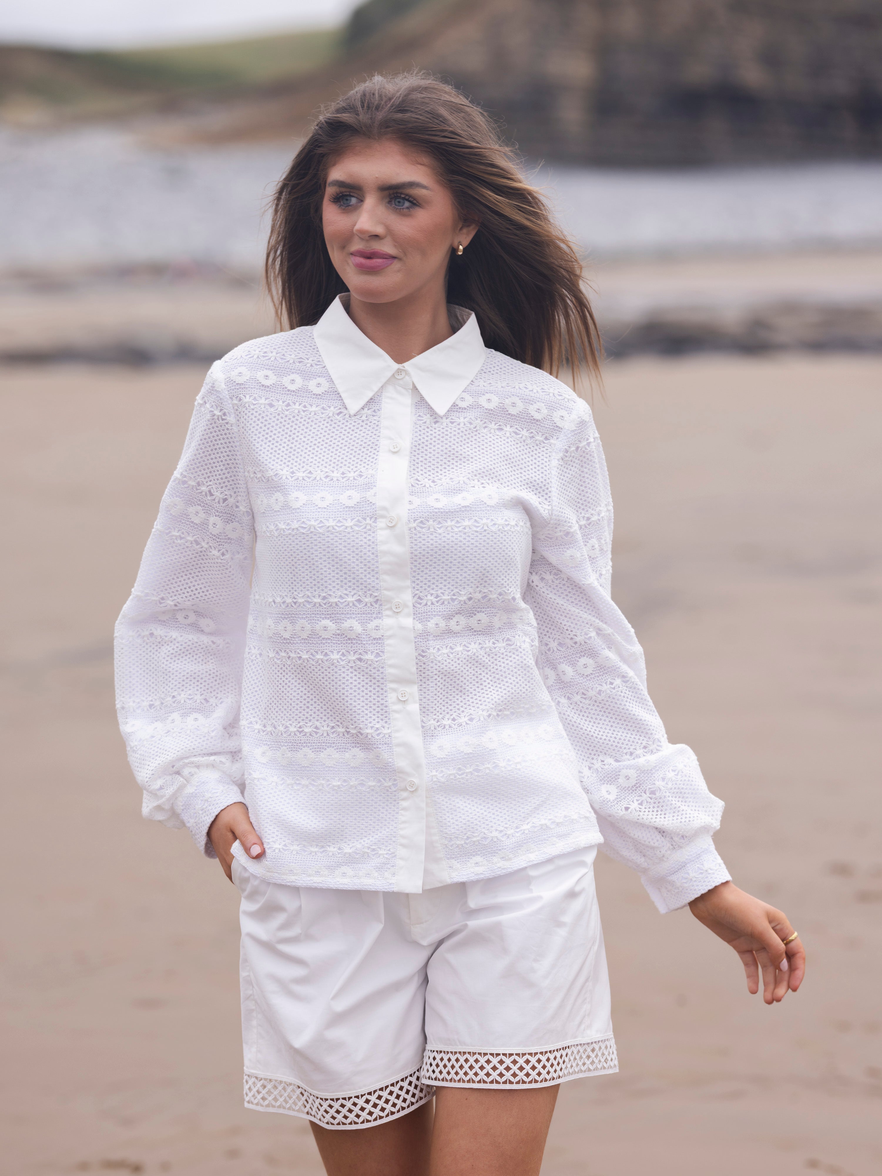 Woman wearing BeReal Wear white lace shirt and shorts on a beach.